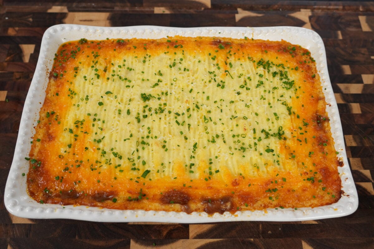 Baked shepherd's pie in a casserole dish with golden Gruyere cheese crust and fresh herb garnish