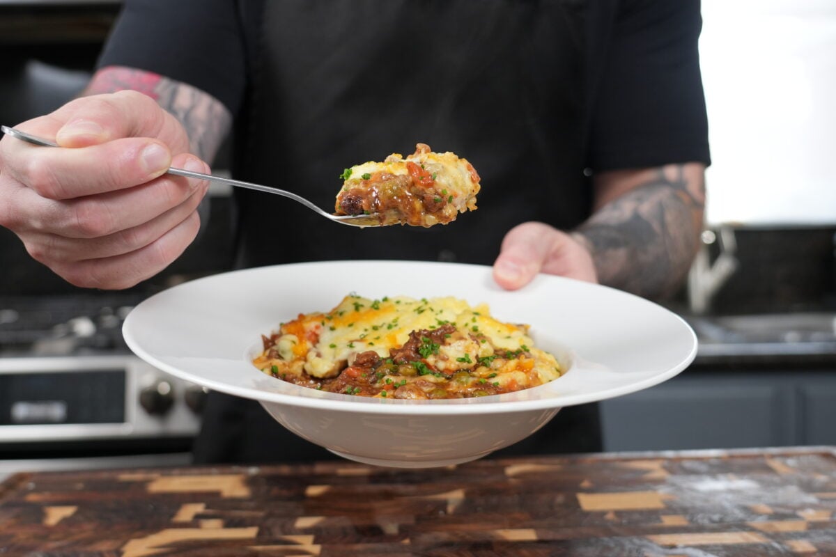 Shepherd's pie recipe served in a bowl with a fork lifting a bite showing layers of meat filling and creamy mashed potatoes