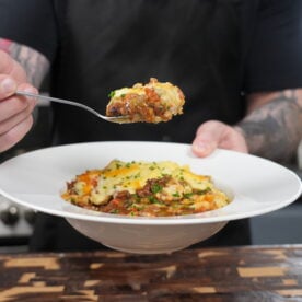 Shepherd's pie recipe served in a bowl with a fork lifting a bite showing layers of meat filling and creamy mashed potatoes