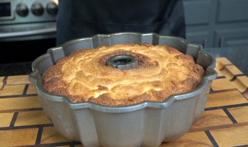 Pouring lemon cream cheese glaze over warm pound cake