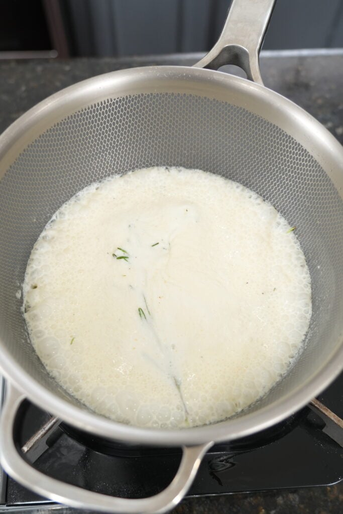 Heavy cream infusing with fresh rosemary sprig on the stovetop