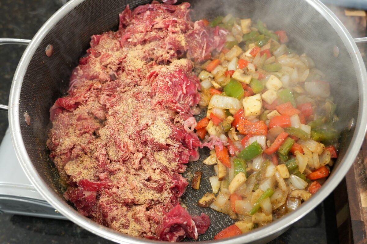 seasoned shaved ribeye cooking in a cast iron skillet