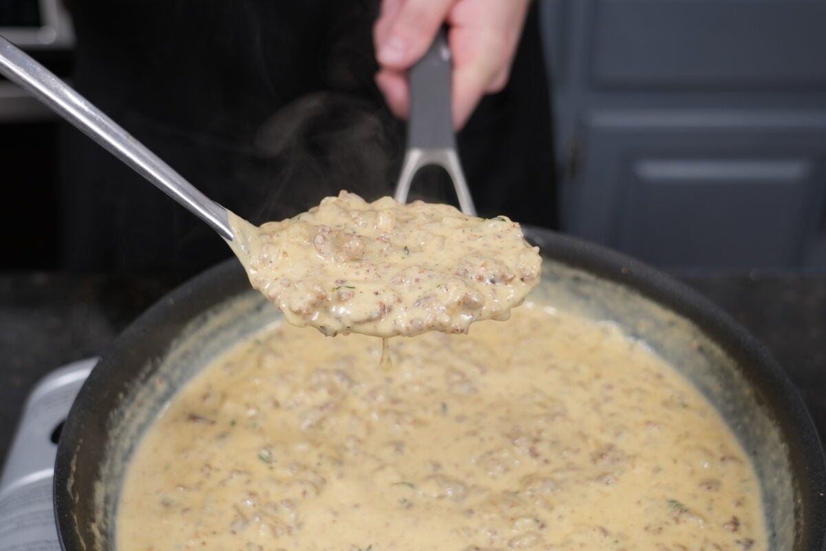 Close-up of homemade biscuits and gravy pulling apart with creamy sausage gravy