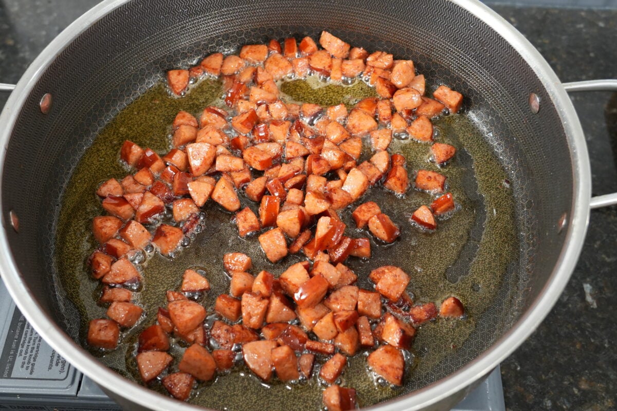 Ground beef and andouille sausage browning in a skillet for dirty cabbage