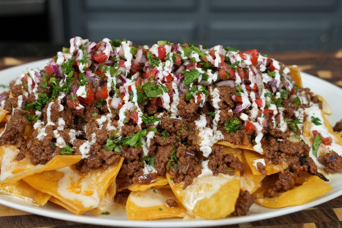 Loaded beef nachos on a white platter topped with ground beef, pico de gallo, and crema