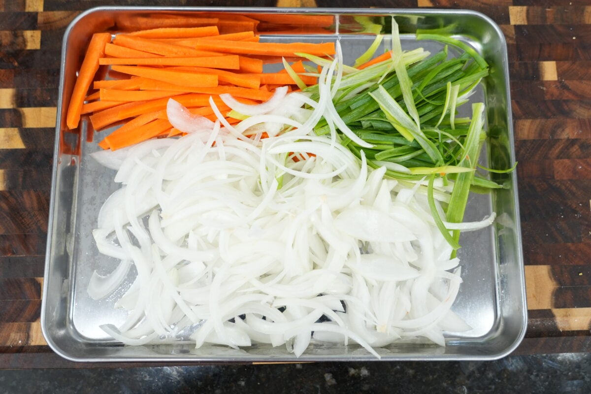 Carrot matchsticks, julienned onion and sliced green onion prepped on a sheet tray