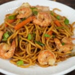 Shrimp lo mein with carrots and green onions plated on a white dish