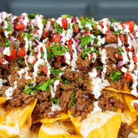 A platter of loaded beef nachos with homemade queso, seasoned ground beef, and pico de gallo
