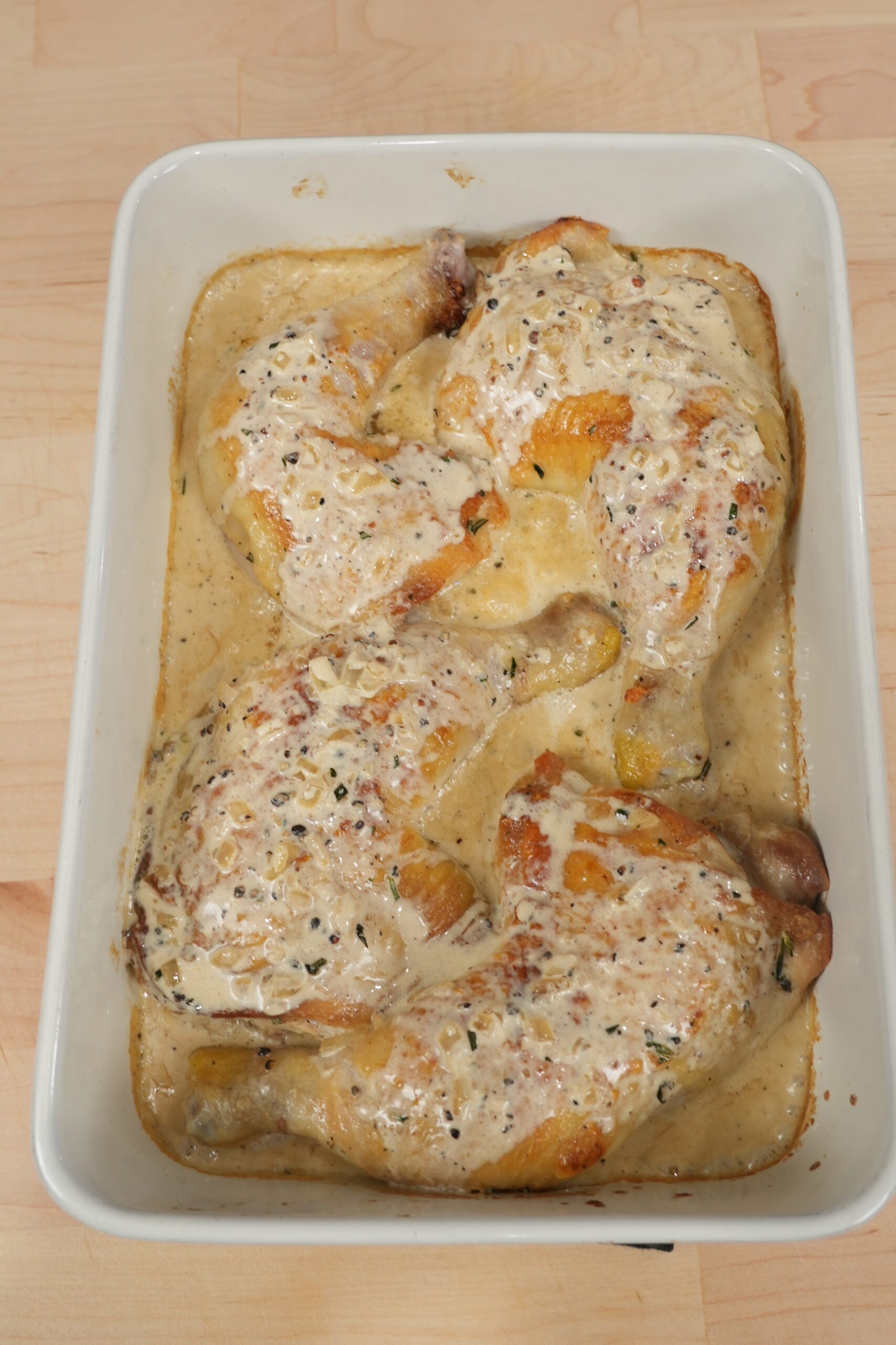 Roasted chicken leg quarters basted with creamy peppercorn sauce in a baking dish