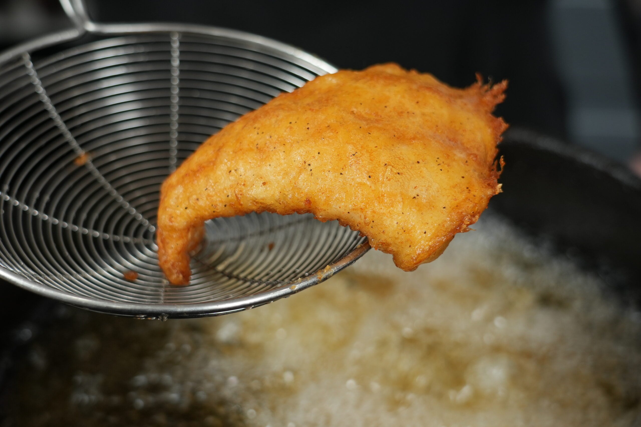 Crispy beer battered cod lifted from hot oil