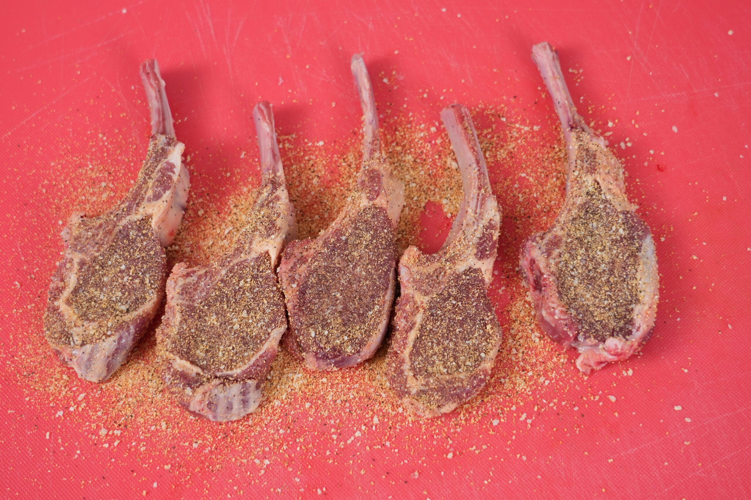 Raw lamb chops coated with seasoning before searing