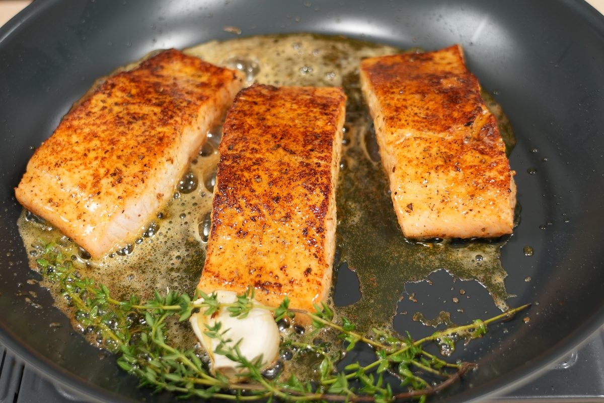 Cajun-seasoned salmon fillets searing in a skillet with butter and herbs