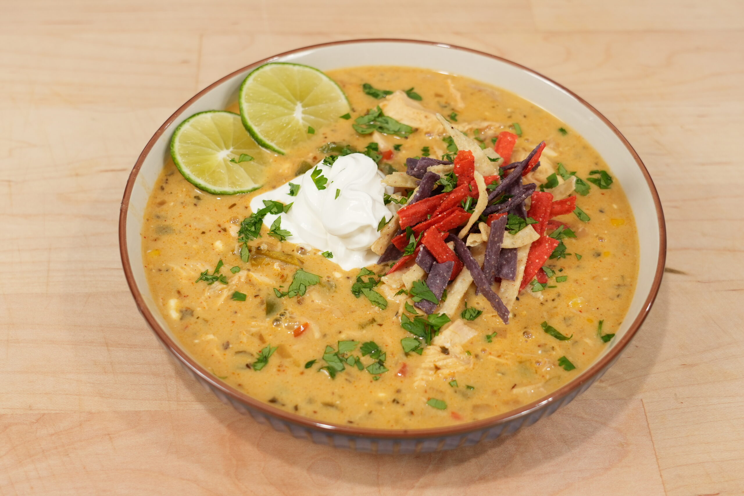 Bowl of creamy white chicken chili with rotisserie chicken, white beans, corn, lime, sour cream, and tortilla strips