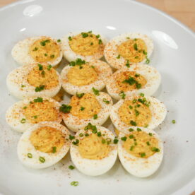Classic deviled eggs topped with paprika and chopped chives on a white serving plate