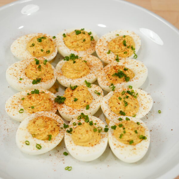 Classic deviled eggs topped with paprika and chopped chives on a white serving plate