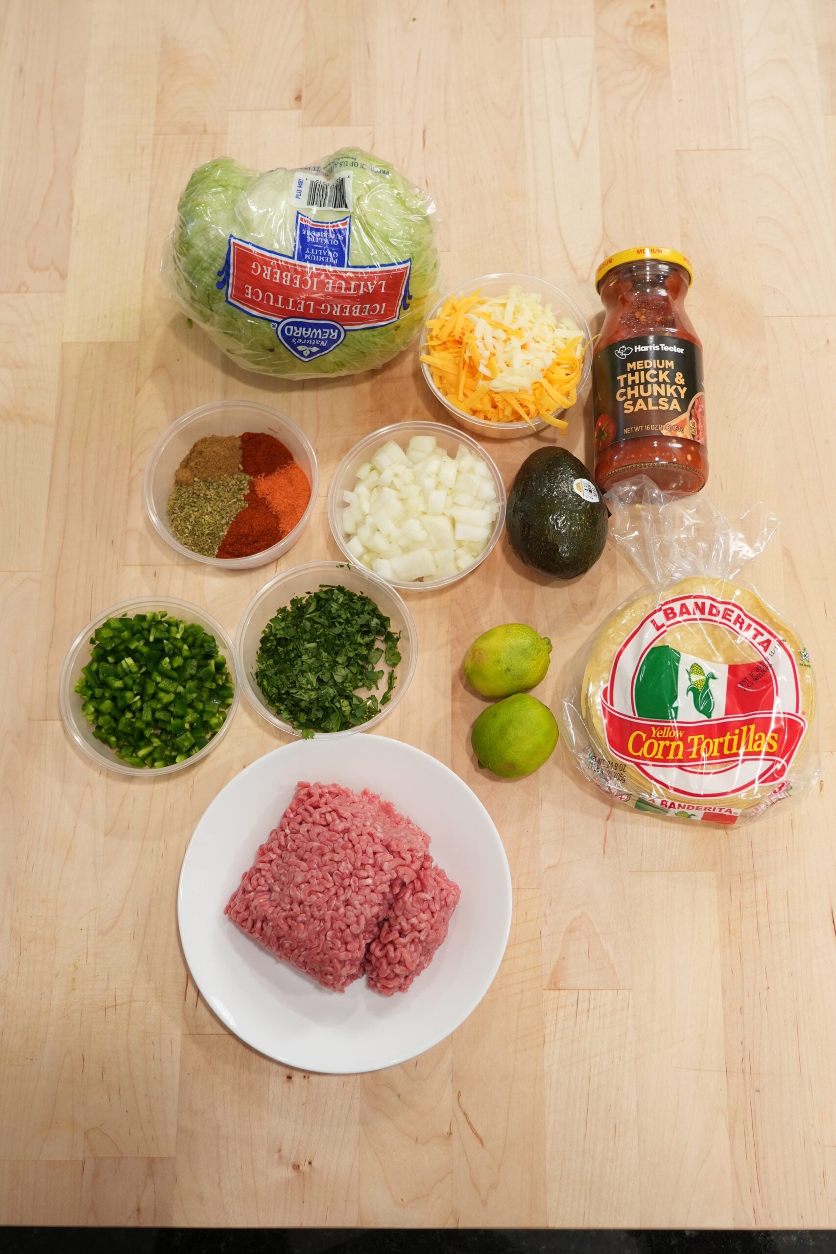 Ingredients laid out for crispy beef tacos, including ground beef, corn tortillas, shredded cheese, onions, jalapeños, seasonings and toppings