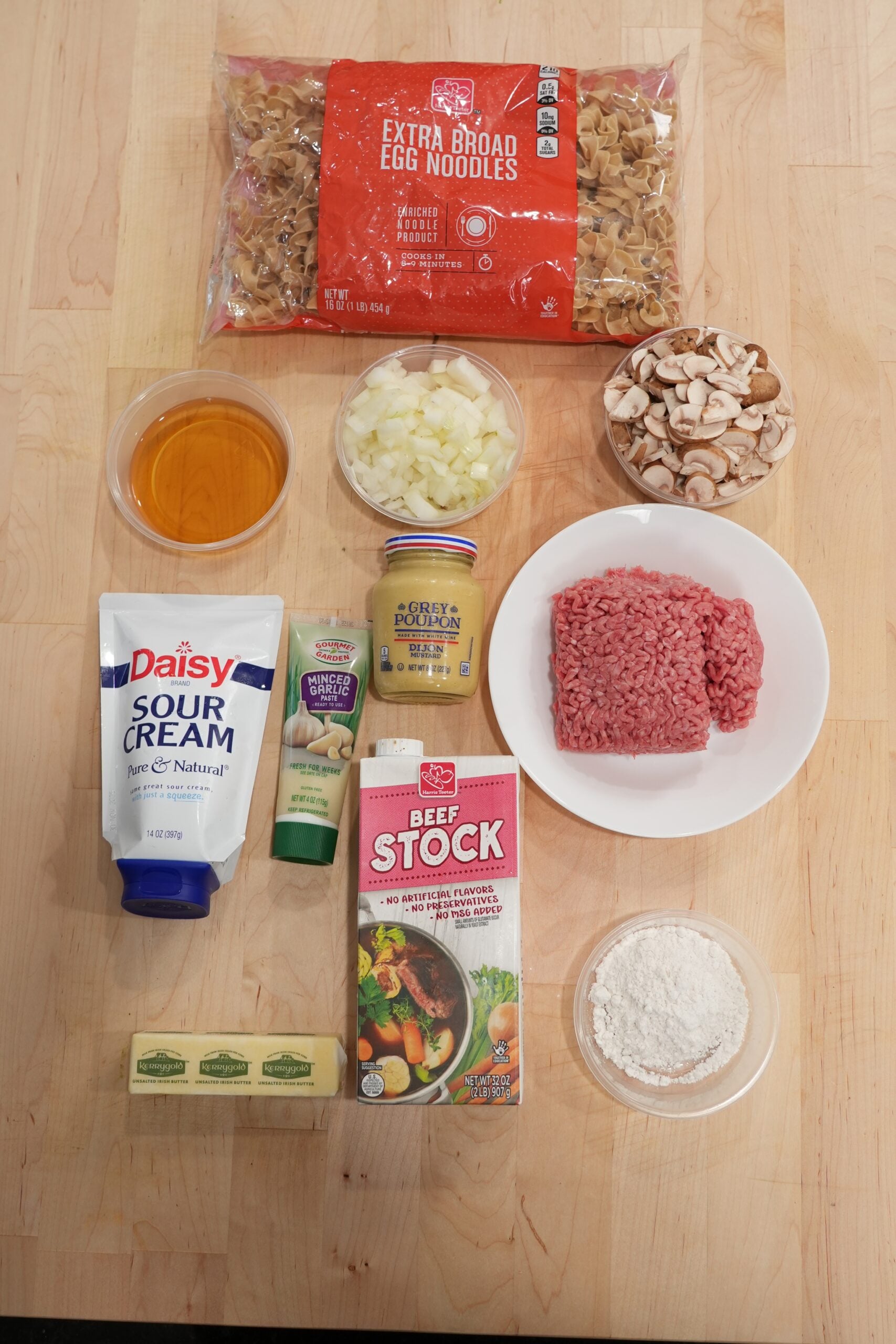 Ingredients for ground beef stroganoff laid out with beef, mushrooms, noodles, stock, sour cream and seasonings