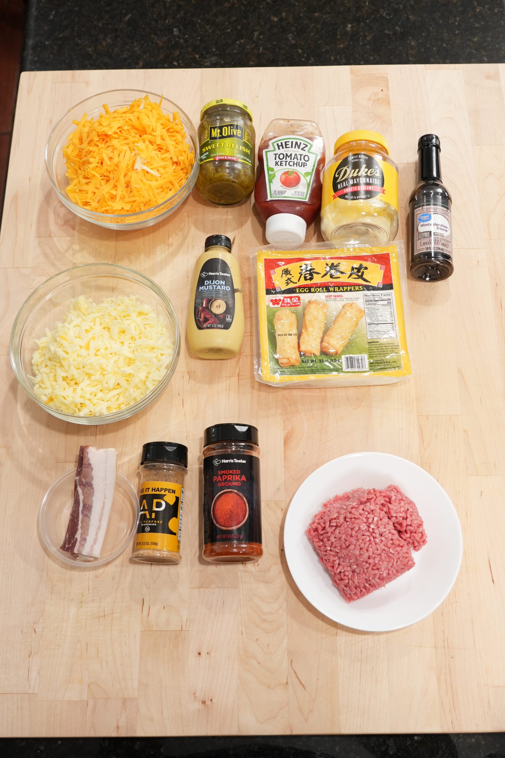 Ingredients for bacon cheeseburger egg rolls and burger sauce laid out on a board