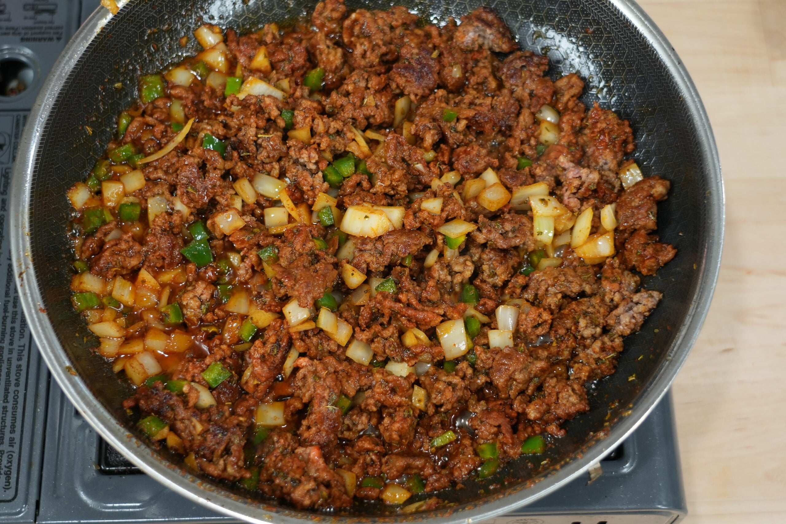 Seasoned ground beef cooking with diced onions and peppers for crispy tacos
