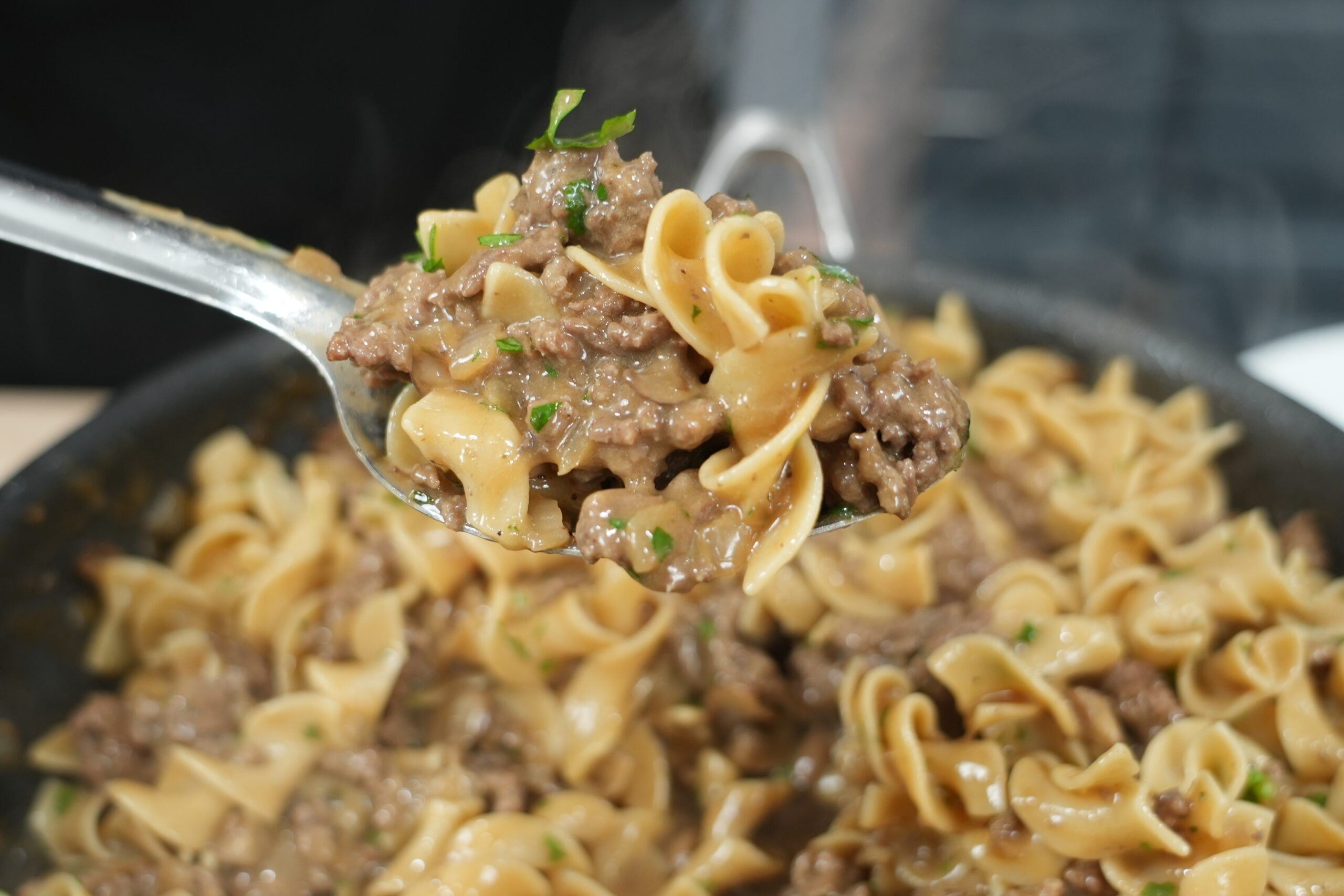 Forkful of creamy ground beef stroganoff and egg noodles above the pan