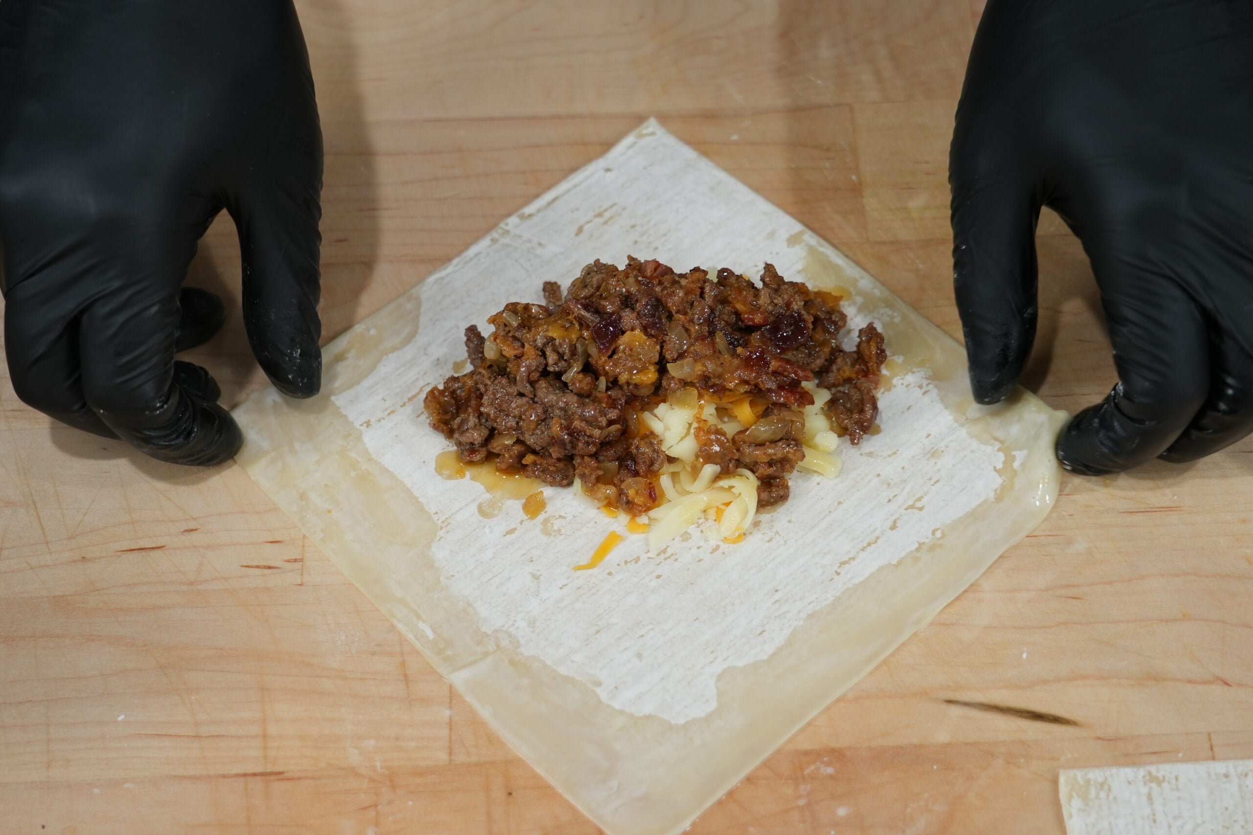 Beef and cheese filling being wrapped in an egg roll wrapper