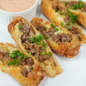 Finished bacon cheeseburger egg rolls cut open with burger sauce