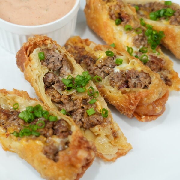 Finished bacon cheeseburger egg rolls cut open with burger sauce