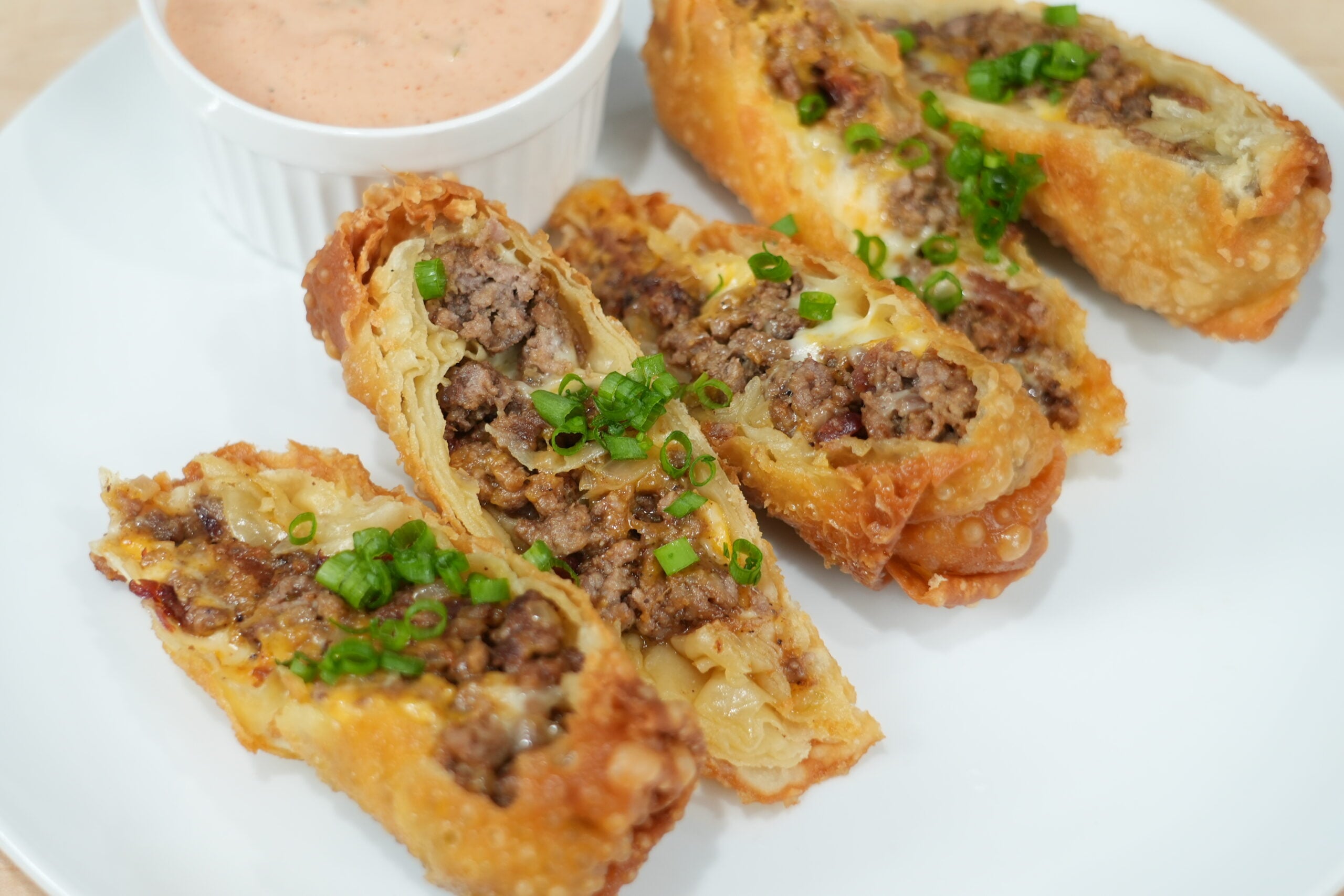 Finished bacon cheeseburger egg rolls cut open with burger sauce
