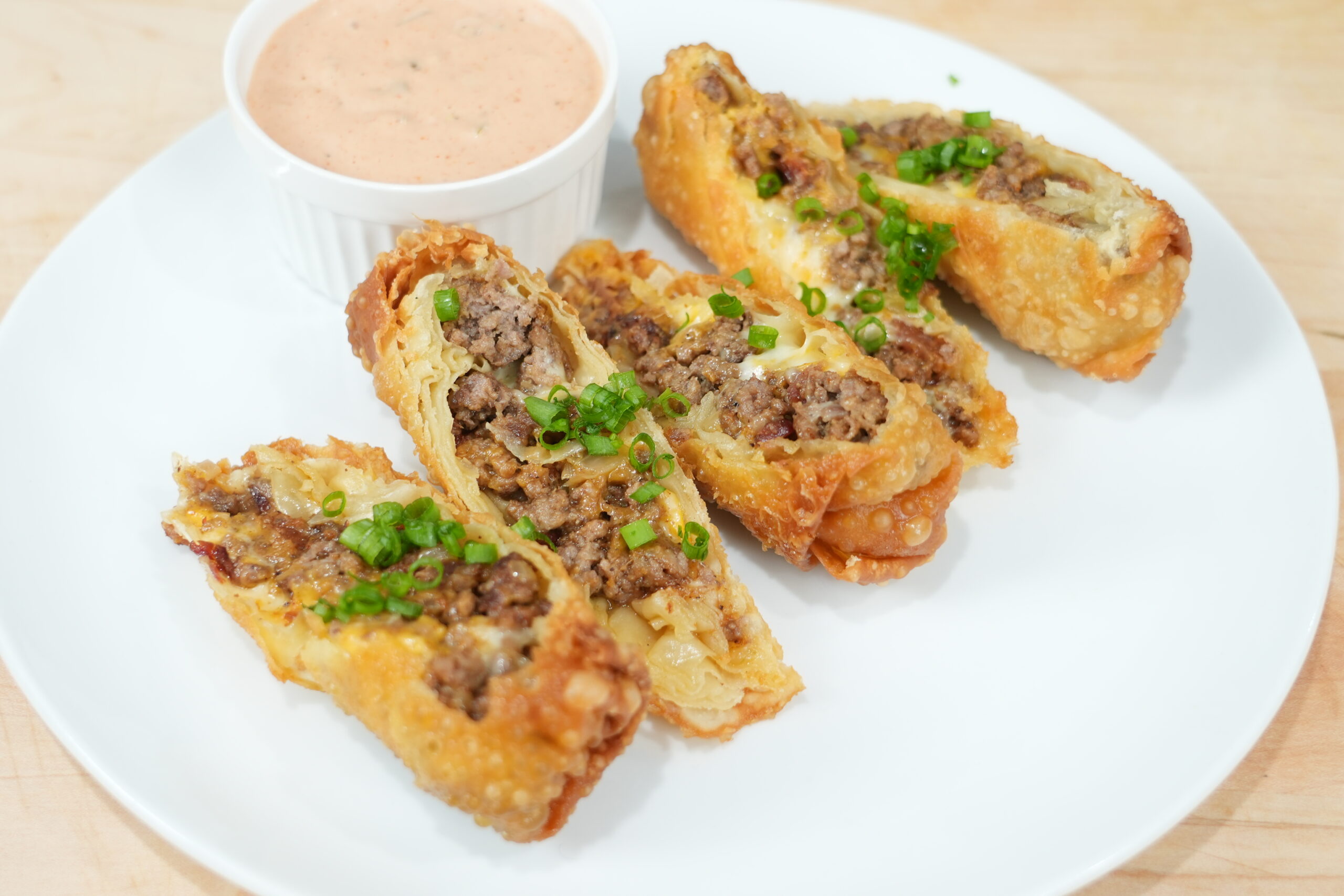 Bacon cheeseburger egg rolls cut open with burger sauce