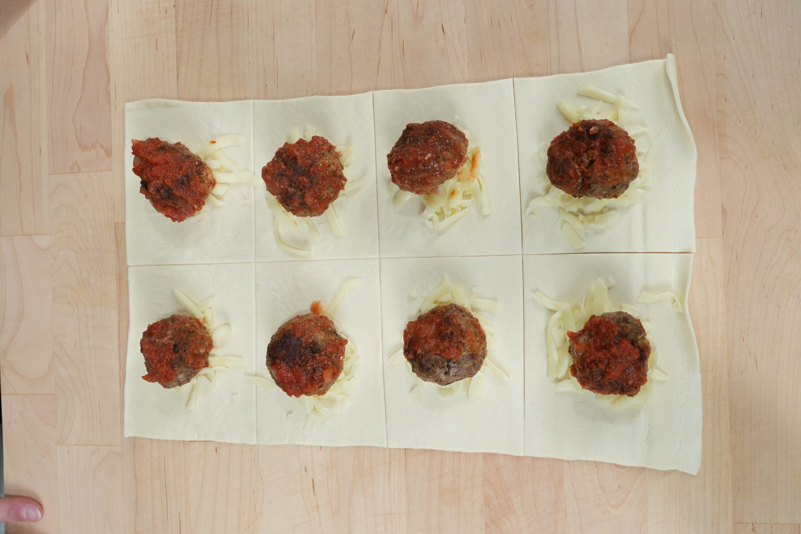 Cooked meatballs and mozzarella arranged on squares of pizza dough