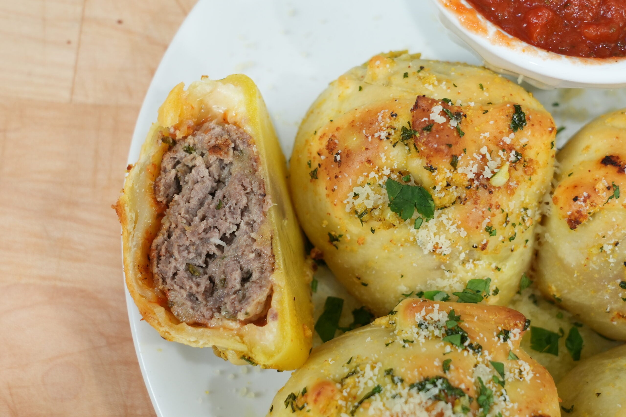 Cut-open garlic knot showing the meatball filling beside marinara
