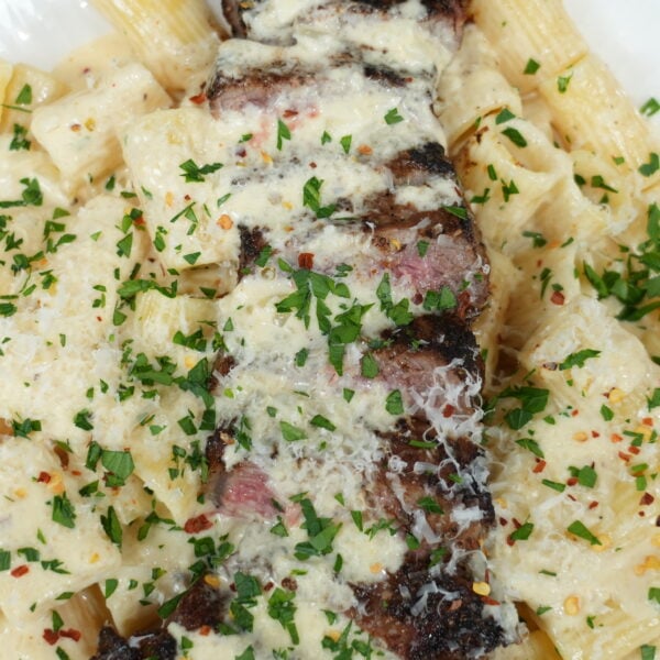 Creamy Cajun steak pasta topped with sliced steak and Parmesan